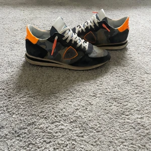 Camouflage sneakers från Philippe Model - Snygga sneakers från Philippe Model i ett coolt camouflage-mönster med orangea detaljer.  storlek 42, hör av dig vid fler frågor och funderingar pris går att diskutera vid snabb affär  