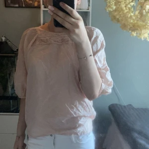 Ljusrosa blus från Wera - Supersöt ljusrosa blus från Wera med avslappnad passform och trekvartsärmar. Blusen har fina veckdetaljer upptill vid halsringningen och är gjord i ett tunt, luftigt material som känns skönt mot huden. Perfekt för dig som gillar en romantisk och enkel stil.