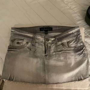 Grå jeanskjol med nitar - Säljer en grå, kort jeanskjol från stradivarius med slitna kanter och coola nitar på fickorna. Kjolen har klassisk femficksdesign, knapp och dragkedja framtill samt snygga detaljer på bakfickorna. Perfekt för dig som gillar en edgy och avslappnad stil. Lågmidjad