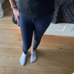 Mörkblå ridbyxor med dragkedjor - Säljer ett par mörkblå ridbyxor med hög midja och tight passform. Byxorna har förstärkta partier på insidan av benen och praktiska dragkedjefickor framtill. Perfekta för dig som gillar ridning och vill ha bekväma och snygga byxor i stretchigt material.