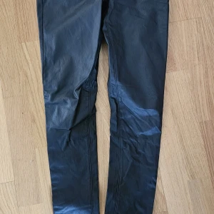 Svarta skinny byxor i skinnimitation - Snygga svarta byxor i skinnimitation med skinny passform. De har klassisk femficksdesign och smala ben som sitter tight hela vägen ner. Perfekta för dig som vill ha en edgy och stilren look.