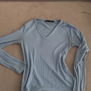 Ljusblå ribbad långärmad tröja - Superskön ljusblå långärmad tröja från Bik Bok med v-ringning. Tröjan är ribbad och har en slim passform som sitter snyggt på kroppen. Perfekt att styla med jeans eller kjol för en chill look.