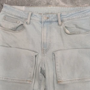 Ljusblå cargojeans från H&M - Ljusblå cargojeans från H&M med regular fit. Byxorna har stora fickor på benen, klassiska femficksdetaljer och bälteshällor. Tillverkade i jeansmaterial och passar perfekt för en avslappnad streetstil.