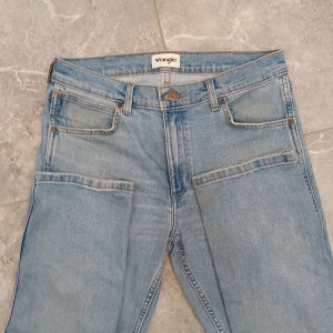 Wrangler Greensboro ljusblå jeans W32 L34 - Säljer ett par ljusblå Wrangler Greensboro jeans med klassisk femficksdesign och snygga kontrastsömmar. Jeansen har raka ben, normal passform och är tillverkade i bomullsdenim. Perfekta för dig som gillar en avslappnad och tidlös look.