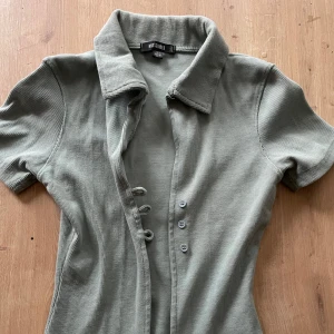 Ljusgrön ribbad kortärmad skjorta, Missguided - Snygg grå ribbad skjorta från Missguided med krage, korta ärmar och knappar framtill. Klänningen har en figurnära passform och är tillverkad i mjuk bomull. 