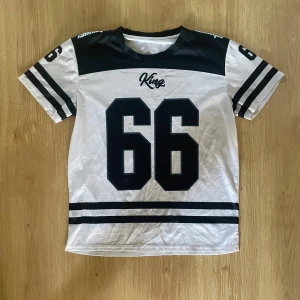 Vit-svart Jersey Nr 66 - Jersey från King i vitt och svart med stora siffran 66 framtill och coola ränder på ärmar och nederkant, perfekt för dig som gillar streetwear och liknande stilar 🙏🏼 Size: M. Skavanker visas på sista bilden 