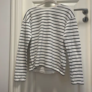 Randig långärmad tröja från Lindex - Vit långärmad tröja från Lindex med svarta ränder. Tröjan har en klassisk rund halsringning och är gjord i mjuk bomull❤️passar perfekt till både sommaren och hösten med en kjol eller ett par jeans