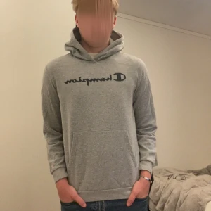 Grå hoodie från Champion  - Säljer en grå hoodie från Champion i storlek XL. Tröjan har svart Champion-logga på bröstet, huva och en stor magficka. Perfekt för dig som gillar en enkel och clean stil. Mjuk insida och klassisk passform. Storlek xl i barn motsvarar xs i herr