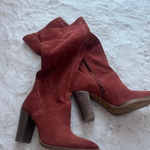 Rostbruna mockastövlar från Bronx - Snygga stövlar i rostbrun mocka från Bronx med spetsig tå och hög klack. Stövlarna har dragkedja på insidan och en chunky träfärgad klack som ger extra attityd. Perfekta för dig som vill sticka ut med en cool och trendig look.
