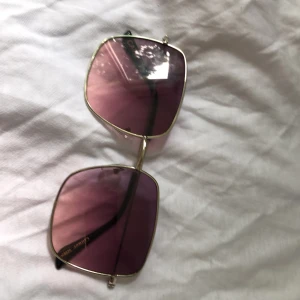 Stora fyrkantiga solglasögon med lila ton - Snygga solglasögon från Ginatricot med stora fyrkantiga glas i lila ton och tunna guldfärgade metallbågar. Sköna näskuddar och svarta skalmar. Perfekt accessoar för en cool look i sommar.