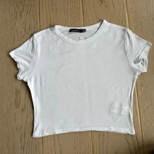 Vit croppad t-shirt  - Enkel och fräsch vit croppad t-shirt från Boohoo. Modellen är tight med korta ärmar. Perfekt till jeans eller kjol för en clean look. Gjord i mjuk bomull som känns skön mot huden.