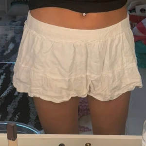 Vita volangshorts med resårmidja - Superfina vita shorts med volangdetaljer och bred resår i midjan. De är luftiga och har en flowy passform som ger en skön och avslappnad vibe. Perfekta för varma dagar och enkla att matcha med crop tops eller linnen.