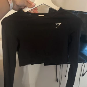 Svart croppad långärmad tröja Gymshark - Säljer en svart croppad långärmad tröja från Gymshark med deras ikoniska logga på bröstet. Tröjan är i stretchigt material som passar perfekt till träning