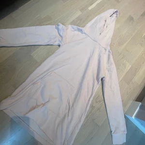 Ljusrosa hoodie med huva och ficka - Lång och oversized ljusrosa hoodie med stor huva och magficka. Tröjan har långa ärmar och är tillverkad i mjuk bomull.