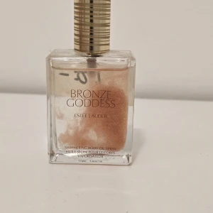 Bronze Goddess Shimmer Oil - Bronze Goddess Shimmering Body Oil Spray från Estée Lauder ger huden en snygg, solkysst glow med guldiga och bronsiga skimmerpartiklar. Kommer i en lyxig glasflaska med guldfärgad spraykork. Perfekt för att boosta lystern på kroppen.