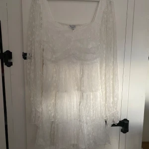Vit spetsklänning från Bubbleroom - Superfin vit kortklänning från Bubbleroom med långa ärmar i spets och volangdetaljer. Klänningen har fyrkantig ringning och blommigt spetsmönster. Den är aldrig använd, köpt från bubbleroom (studentklänning). Nypris var 999kr