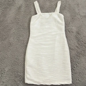 Vit kort klänning med struktur - Snygg vit kortklänning med vågig struktur. Klänningen har en figurnära passform och är perfekt för dig som gillar en stilren look med lite extra textur. Enkel men ändå unik design som sticker ut.