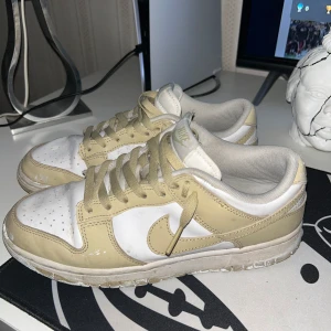 Nike Dunk Low i beige och vitt - Nike Dunk Low sneakers i en clean beige och vit färgkombo. Klassisk siluett med rund tå, snörning och platt sula. Ovandel i skinn och syntet, perfekt för dig som gillar streetwear och vill ha en stilren look.