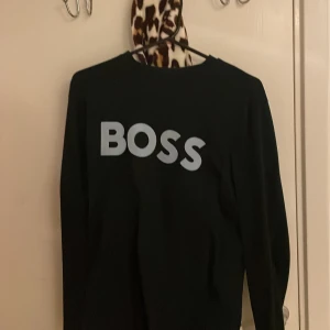 Svart långärmad tröja från BOSS - Svart långärmad tröja från BOSS med stor vit logga framtill. Enkel och stilren design med rund halsringning. Perfekt för dig som gillar klassiska plagg med tydlig branding.passar även M