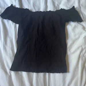 Svart offshoulder topp Gina Tricot  - Svart ribbad offshoulder topp från Gina Tricot i storlek XS. Toppen har korta ärmar och stretchigt material.
