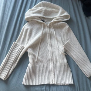 Vit ribbad hoodie från Gina Tricot - Superfin vit hoodie från Gina Tricot i ribbstickat material. Tröjan har dragkedja framtill, huva med snörning och långa ärmar. Perfekt för dig som gillar en clean och stilren look med lite extra cozy vibes.