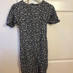 Svartvit blommig kortklänning Bik Bok - Supersöt svart kortklänning från Bik Bok i storlek XS med vitt blommigt mönster. Klänningen har korta puffärmar och en figurnära passform. Perfekt för dig som gillar en feminin och trendig stil. Med dragkedja i ryggen