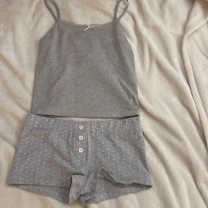 Grått pyjamas sett från  Gina Tricot - Super gulligt pyjamas sett ifrån gina tricot. Toppen har spets med en liten rosett. Shortsen har prickar och vita knappar.