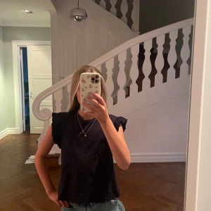 Marin blå volangärmad topp - En marin blå  topp med volangdetaljer på ärmarna. Modellen är ärmlös med en rak passform och rund halsringning. Perfekt att styla med jeans eller kjol för en enkel men snygg look.