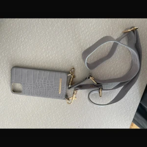 Grå axelväska/telefonväska från Ideal of Sweden IPhone 11 Pro MAX  - Snygg grå axelväska/telefonväska från Ideal of Sweden med krokodilpräglat mönster och guldfärgade detaljer. Väskan har justerbar axelrem och passar perfekt för mobilen. Stilren och trendig accessoar för dig som vill ha händerna fria.