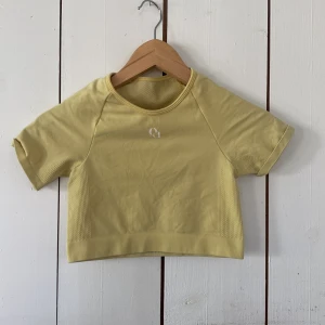 Gul croppad träningstopp own|u - Väldigt strechig croppad gul träningstopp från own|u med korta ärmar och rund hals. Toppen har ventilerande meshdetaljer på sidorna och ryggen samt en liten vit own|u -logga framtill. Perfekt för gymmet eller löprundan. (Orginal pris 500kr)