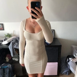 Ribbad beige kortklänning H&M Divided - Supersnygg ribbad kortklänning i beige från H&M Divided. Klänningen har lång ärm, tight passform och en snygg fyrkantig ringning. Perfekt för dig som gillar en enkel men trendig stil.