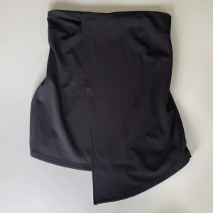 Svart bandeau från Bik Bok - Säljer en svart bandeau tubtopp från BikBok i storlek M. Toppen är axelbandslös och har en snygg asymmetrisk nederkant. Den har ett silikonband för att hålla toppen uppe. Lappen där det står att den är från BikBok har nästan lossnat, i övrigt är den i jättebra skick!