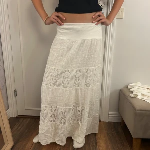 Vit långkjol med spetsdetaljer - Superfin vit långkjol med bred midjeresår och inslag av spets i två sektioner. Kjolen är luftig och har en bohemisk vibe med sitt tunna bomullstyg och de snygga spetsdetaljerna som ger extra stilpoäng.