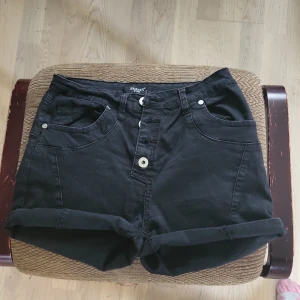 Svarta shorts från Sisters Point XS - Svarta shorts från Sisters Point i bomull med upprullade benslut och klassisk femficksdesign. De har knapp och dragkedja framtill samt bälteshällor. Perfekta för en chill sommarlook.
