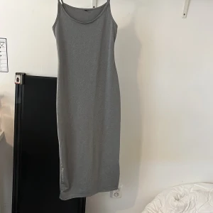 Grå ärmlös långklänning - Enkel och stilren grå långklänning med smala axelband och rak passform. Klänningen är ärmlös och har en mjuk känsla, perfekt för en avslappnad look. Passar lika bra till sneakers som sandaler.