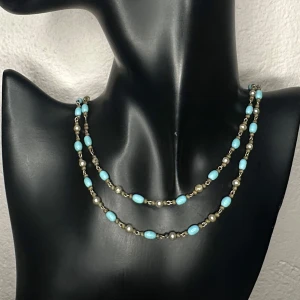 Vackert vintagehalsband med turkosa pärlor & mässingsdetaljer - Retro - 50-tal/70-tal - Vackert vintagehalsband från 50/70-talet, inropat på auktion. Halsbandet består av två strängar med turkosblå pärlor, pärlliknande kulor och mässingsfärgade metallpärlor med fin patina. Jag vet inte om pärlorna är glas eller naturstenen turkos. Eftersom jag inte kan garantera materialet säljer jag det billigt som vintage glashalsband. Ca 47 cm. Ett tidstypiskt smycke med en härlig retrolook.  Prutning accepteras inte, men jag erbjuder bra rabatt vid köp av flera saker. Jag rensar smyckesskrin 