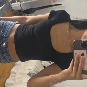 Svart croppad topp från H&M Divided - Svart croppad topp från H&M Divided med korta ärmar och djup, rundad urringning. Sitter tight och har en enkel, stilren look som passar till jeans eller kjol. Mjuk och stretchig i materialet för en bekväm känsla.