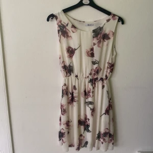 Blommig kortklänning från Hailys - Supersöt kortklänning från Hailys i storlek XL( OBS! är egentligen en xl men liten i storleken så skulle snarare räknas som en M).     Klänningen är vit med stora blommiga mönster i vinröda och rosa toner, har resår i midjan och är ärmlös. Perfekt för sommarens alla tillfällen när du vill känna dig extra fin.