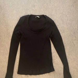 Svart ribbad långärmad tröja - En svart, ribbad långärmad tröja med rund halsringning. Tröjan har en enkel och stilren design som passar perfekt till jeans eller kjol. Materialet är stretchigt och sitter snyggt på kroppen. Perfekt basplagg för garderoben.