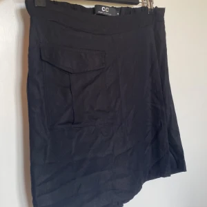 Svart skort från Capri Collection storlek XS - Svart skort (kjol fram/shorts bak) från Capri Collection med en cool ficka framtill och elastisk midja. Kjolen har en enkel, rak passform och är perfekt för dig som gillar minimalistisk stil. Materialet känns mjukt och lätt, och den svarta färgen gör den enkel att matcha med allt.