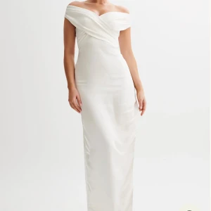 Vit offshoulder balklänning - Elegant vit långklänning med offshoulder-skärning och draperad omlott över bysten. Klänningen har en hög slits framtill. Passar perfekt till balen. Helt oanvänd!