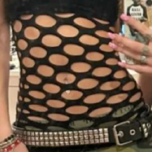 Svart tubtopp med stora hål - Säljer en svart tubtopp i stretchigt syntetmaterial med stora, ovala hål över hela toppen. Toppen är tight och axelbandslös, perfekt för att skapa en edgy och unik look. Passar dig som vill sticka ut och gillar alternativ stil.