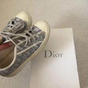 Walk'n'Dior grå sneakers i canvas - Snygga Walk'n'Dior sneakers i grå canvas med Dior-monogram och vita detaljer. Skorna har snörning, rund tå och platt sula med svart stjärndetalj undertill. Perfekta för dig som vill ha en lyxig och trendig vardagssneaker med ikoniskt mönster. Kvittot är digitalt ska försöka hitta men de många år sedan köp💞🌺☺️🌸