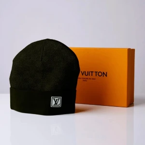 Svart mössa från Louis Vuitton - Stilren svart mössa från Louis Vuitton med klassisk LV-logga framtill. Mössan har en enkel, tidlös design och är perfekt för dig som vill ha en exklusiv accessoar. Materialet ser ut att vara mjukt och bekvämt, perfekt för kyliga dagar.