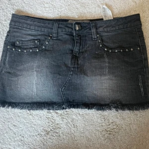 Svart jeanskjol med nitar och frans - Cool svart jeanskjol med slitna detaljer, fransig nederkant och nitar vid fickorna. Säljer endast om man budar bra pris.