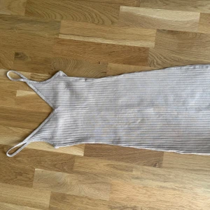 Ljus ribbad kortklänning med smala band - Supersöt ljus kortklänning med smala axelband och ribbad struktur. Klänningen är ärmlös och har en enkel, tight passform som känns både trendig och bekväm. Perfekt för varma dagar när du vill ha något lätt och stilrent.