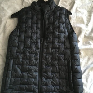 Svart dunväst från Everest - Säljer en svart dunväst från Everest med quiltad design och hög krage. Västen har dragkedja framtill och är lätt vadderad, perfekt att slänga över en hoodie eller tröja när det är kyligt ute.