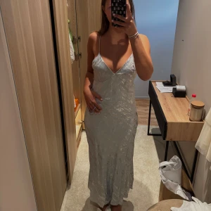 Silverfärgad lång satinklänning - Silver klänning från NAKD med djup rygg. Aldrig använd och har kvar prislappen. Köptes för 600kr