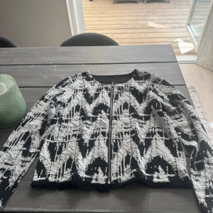 Tröja - Tröja med dragkedja med fransar nertill i vitt och svart.