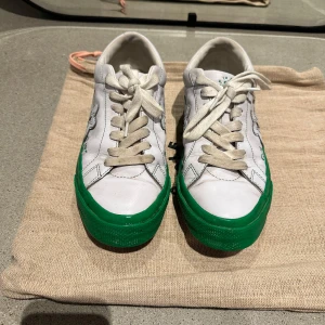 Golf le Fleur x Converse vita sneakers - Unika Golf le Fleur x Converse sneakers i vitt skinn med grön sula och blommig detalj på sidan. Klassisk låg modell med snörning och coola blommor under sulan. Perfekta för dig som vill sticka ut med en streetig vibe.